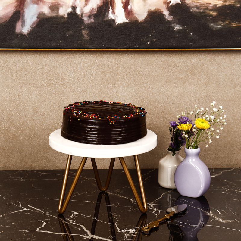 Chocolate truffle cake with rainbow sprinkles on a marble cake stand, styled for a bakery social media campaign